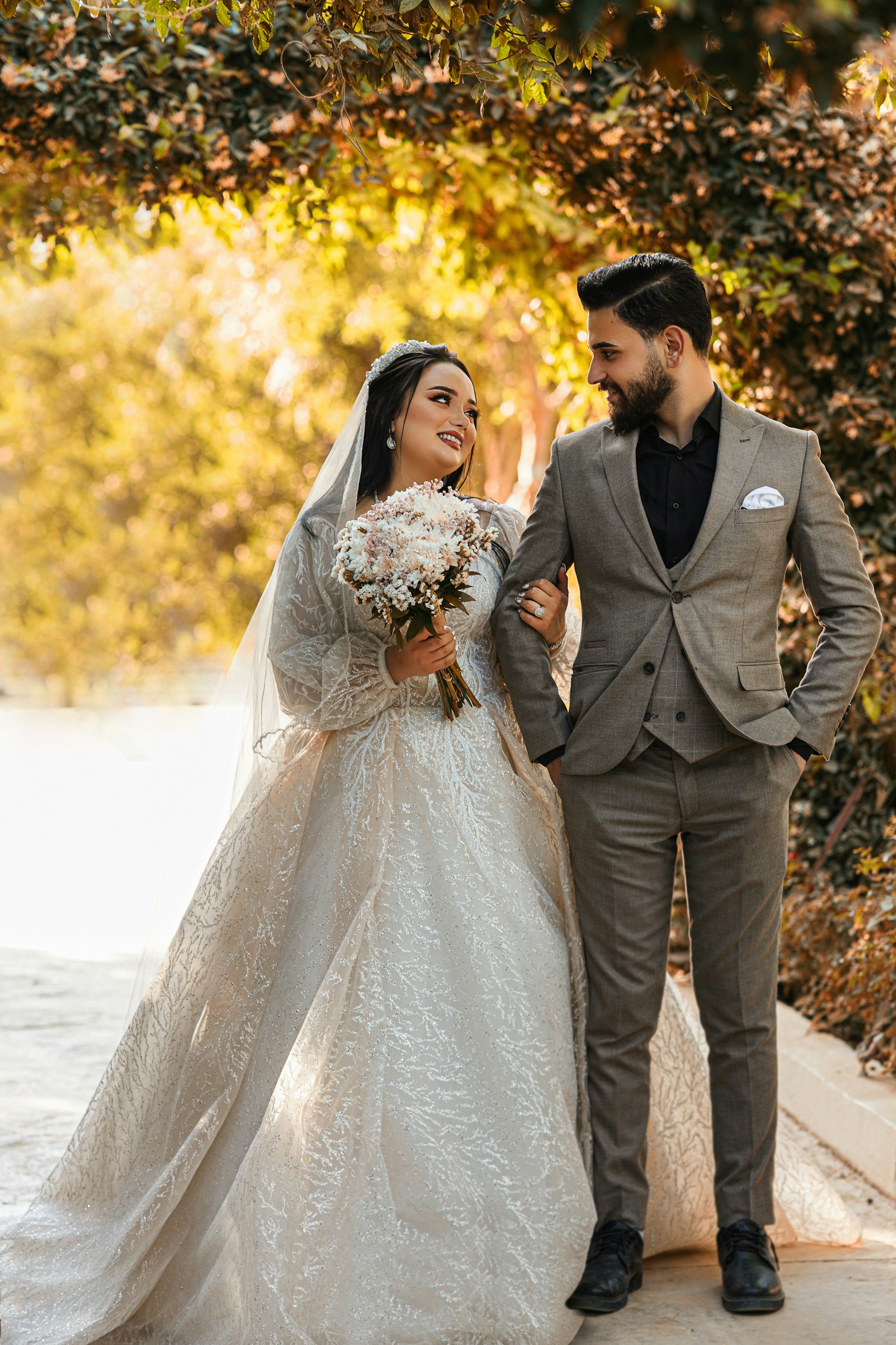 A wedding couple walking together beneath green foliage